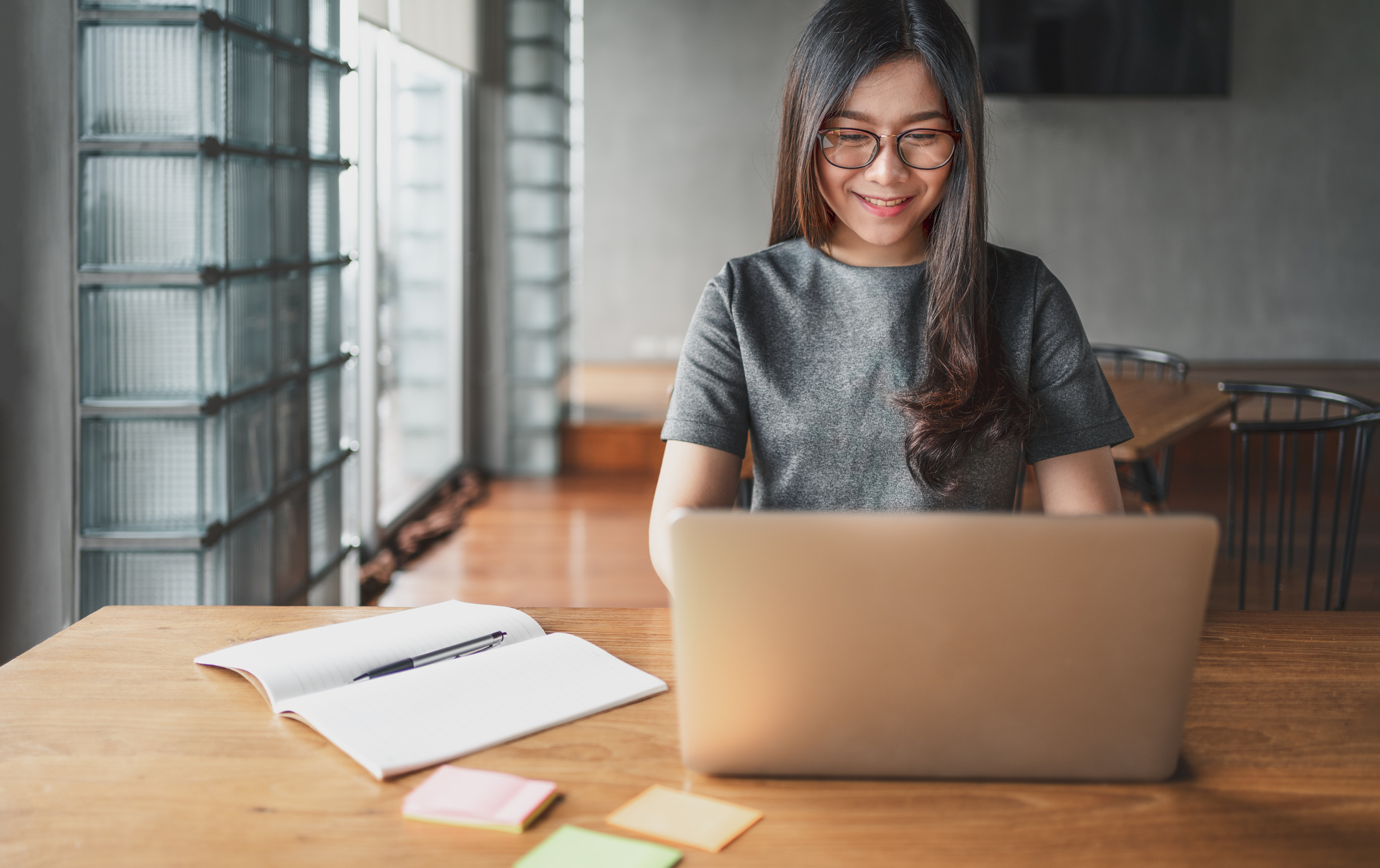 student sitting at a table smiling at her laptop