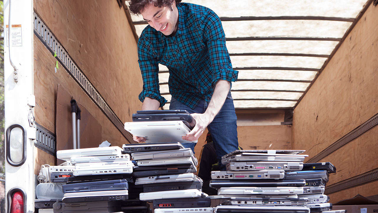 young man handling numerous used laptops