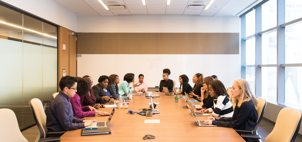 A group of people in a meeting, gathered around a conference table