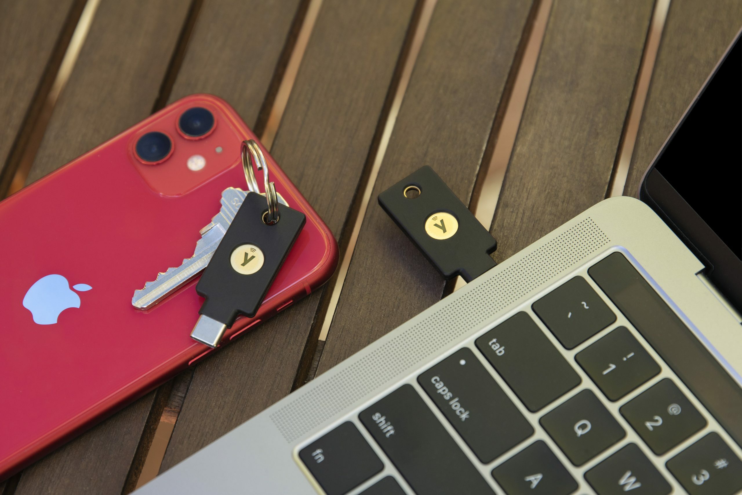 A smartphone and laptop computer wit two Yubico YubiKeys on a deck-like background