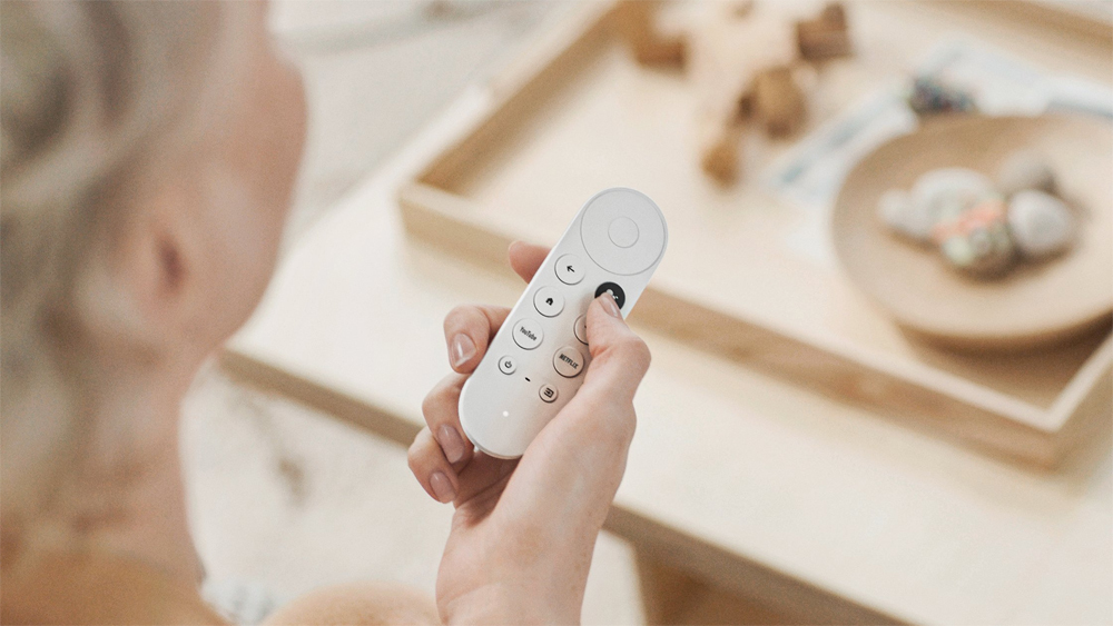 woman holding white Chromecast remote over a coffee table with decorative items on it
