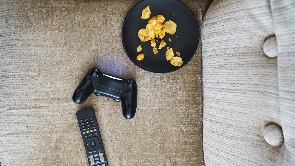 controller and remote control on sofa with bowl of chips sitting nearby
