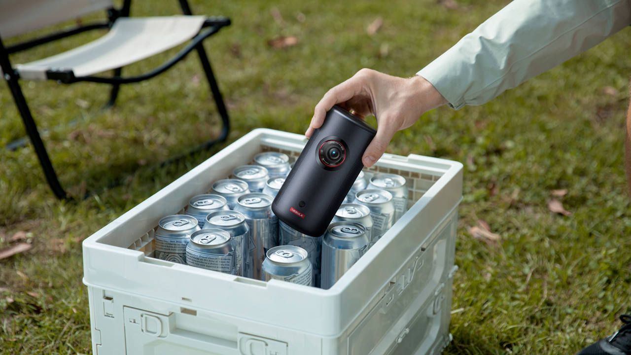 Anker Nebula Capsule 3 Laser projector being held in a hand next to soda cans